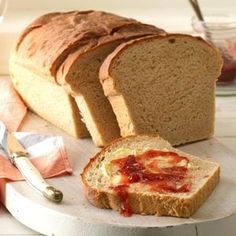 a loaf of bread sitting on top of a cutting board next to sliced bread and jam