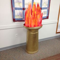 a gold vase filled with red and orange fire extinguishers in front of a flag