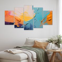 a living room with a white couch and four paintings on the wall in different colors