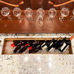 several wine glasses are lined up in a wooden case on a marble countertop next to an assortment of empty wine glasses