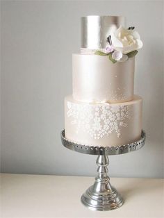 a three tiered wedding cake with white flowers on top and silver trimmings