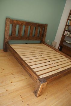 a wooden bed frame sitting on top of a hard wood floor next to a book shelf