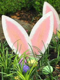 two pink and white bunny ears sitting in the grass next to some easter eggs,