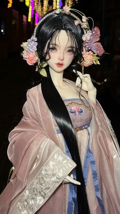 a doll with long black hair wearing a pink dress and holding a flower in her hand