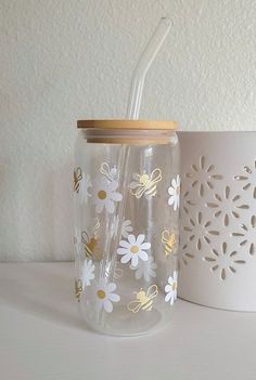 a glass with a straw in it sitting next to a cup that has a flower design on it