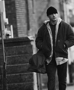 black and white photograph of man walking down the street with his skateboard in hand