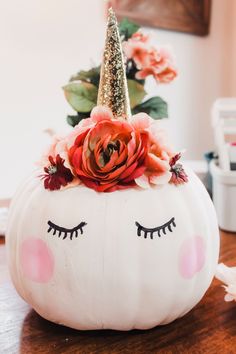 a white pumpkin decorated with flowers and a unicorn's face