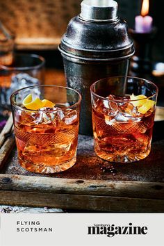 two glasses filled with ice sitting on top of a tray next to a canister