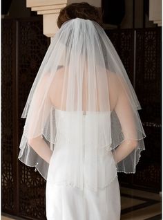 the back of a bride's wedding dress with a veil on her head and shoulder