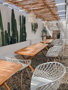 an outdoor dining area with wooden tables and white wicker chairs, hanging cactus plants on the wall