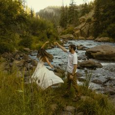 a man and woman standing next to each other in front of a river holding hands