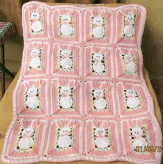 a pink crocheted blanket with white rabbits on the front and back, sitting on a wooden chair