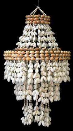 a chandelier made out of shells hanging from a black background with white and brown beads