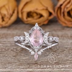 an engagement ring with a pink stone surrounded by white diamonds on a wooden table next to roses