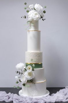 three tiered wedding cake with white flowers and greenery on the top, against a gray background