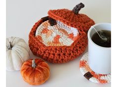 a crocheted basket with two small pumpkins next to it and a coffee cup