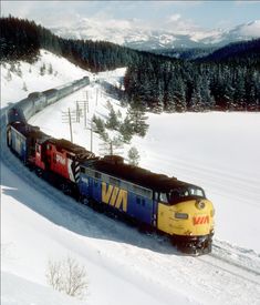 a train is traveling through the snow on its tracks in the country side area with mountains in the background