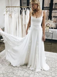 a woman standing in front of a rack of wedding dresses