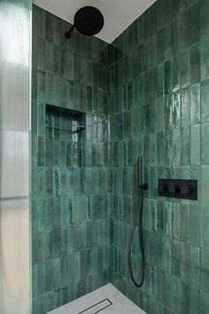 a green tiled shower with black faucet and hand held shower head in the corner