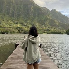 a woman standing on a dock looking out at the water and mountains in the distance