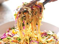 someone is lifting noodles from a bowl with broccoli and carrots on it