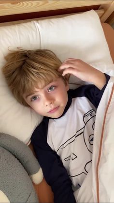 a young boy laying in bed next to a stuffed animal