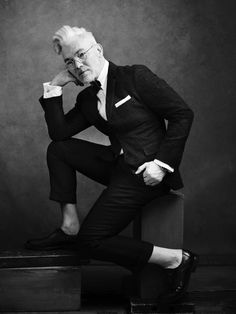 an older man in a suit and tie sitting on top of a wooden box with his hands under his chin