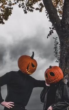 two people wearing pumpkin heads standing next to a tree