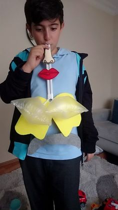 a young boy standing in a living room holding a piece of paper to his mouth