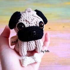 a small crocheted pug dog sitting on top of a persons hand in front of a colorful background