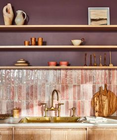 a kitchen with wooden cabinets and pink tile backsplash, brass faucets