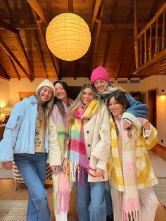 four girls are posing for the camera in a room with wooden floors and ceiling lights