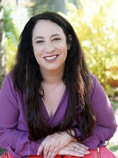 a woman with long hair sitting on a bench smiling at the camera and holding a red purse