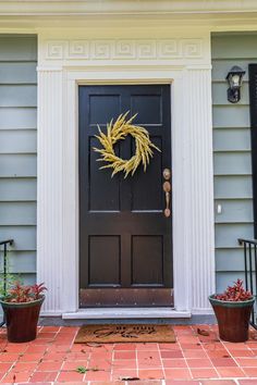 a black front door with a yellow wreath on it and two potted plants outside