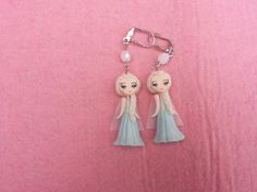 two frozen princesses wearing blue dresses are hanging from a keychain on a pink background