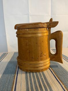 a wooden mug sitting on top of a striped tablecloth with a knife sticking out of it