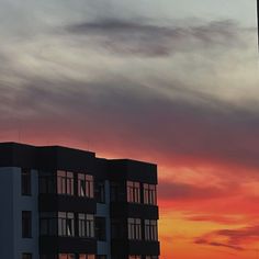 an airplane is flying in the sky over some buildings at sunset or sunrise with clouds