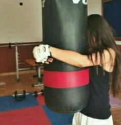 a woman is standing next to a punching bag in a room with red and black mats