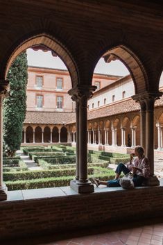 a woman sitting on top of a stone floor next to a building with arches over it