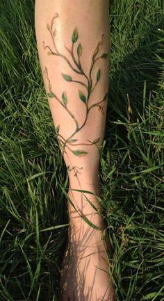 a woman's foot with green leaves on it and grass in the foreground