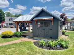 a small shed with a porch and swing chair in the front yard on a sunny day