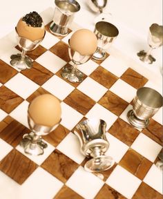 an egg sitting on top of a checkered board with silver cups and spoons