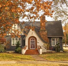 a gray house with white trim and red front door in the fall leaves on the grass