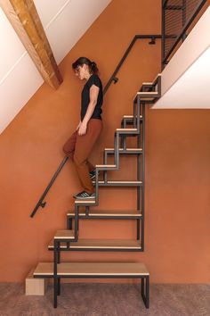 a woman standing at the top of a stair case in front of an orange wall