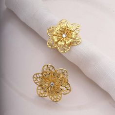 two gold flower napkin rings sitting on top of a white cloth