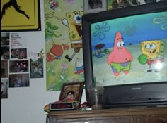 a television sitting on top of a wooden dresser next to a wall covered in pictures