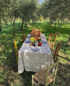 the table is set with flowers and plates on it in an apple orchard, surrounded by trees