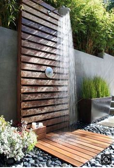 an outdoor shower with wooden slats and water flowing from the faucet to the ground