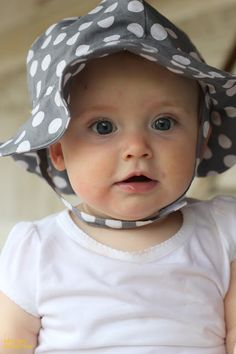 a baby wearing a gray and white polka dot sun hat on top of her head