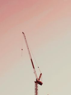 a crane is standing on top of a building under a pink cloudless sky,